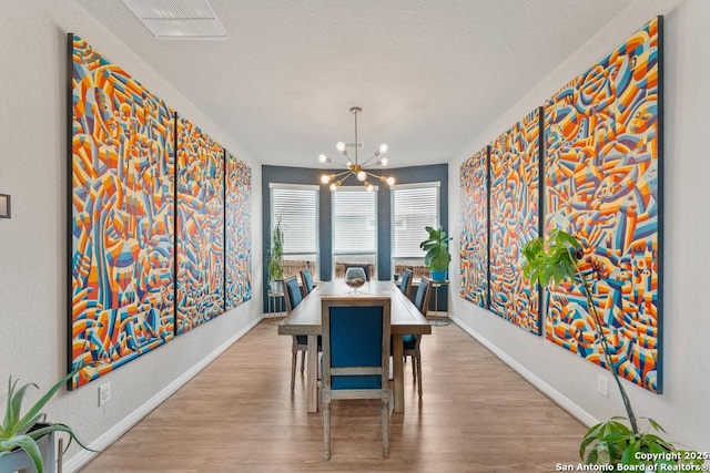 dining room featuring an inviting chandelier, wood finished floors, a textured ceiling, and baseboards