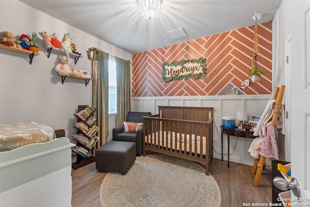 bedroom with an accent wall, wood finished floors, and wallpapered walls