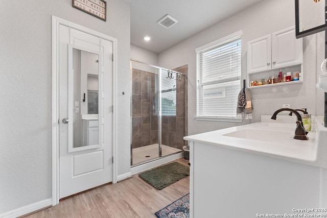 full bath featuring wood finished floors, visible vents, vanity, baseboards, and a stall shower
