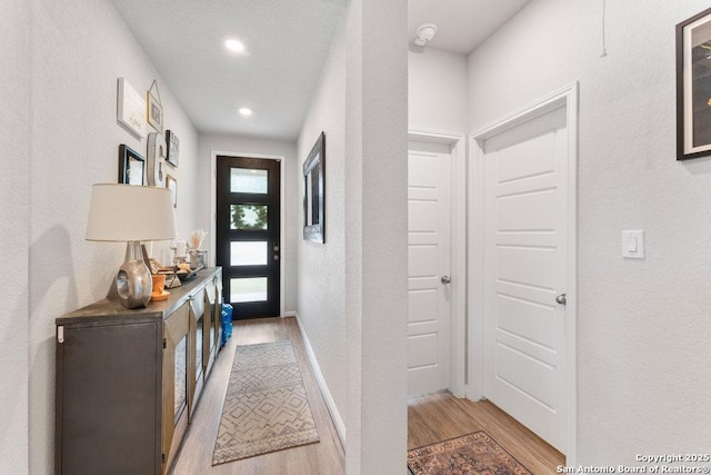 interior space featuring baseboards, recessed lighting, a textured wall, and light wood-style flooring