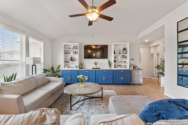 living room featuring light wood finished floors, baseboards, built in features, lofted ceiling, and a ceiling fan