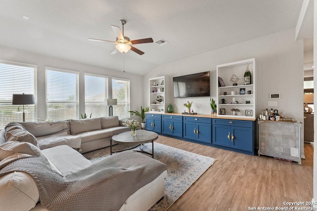 living room with light wood finished floors, visible vents, a bar, lofted ceiling, and a ceiling fan
