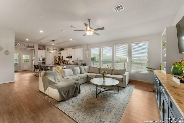 living area with baseboards, visible vents, light wood-style floors, and ceiling fan