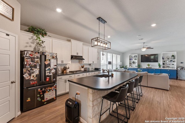 kitchen featuring a sink, dark countertops, freestanding refrigerator, light wood-style floors, and a ceiling fan