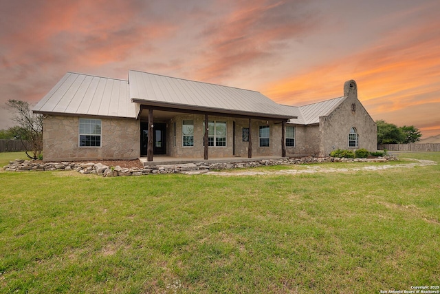 view of front of house with stone siding, a standing seam roof, a front lawn, and metal roof