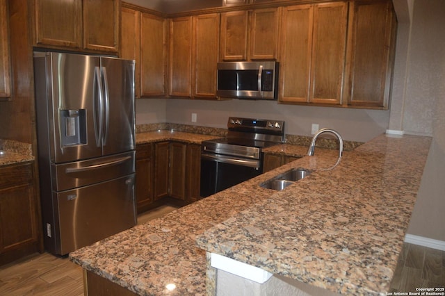 18687 Rolling Mdw, Lytle, TX 78052 - kitchen featuring a peninsula, a sink, brown cabinets, light stone counters, and appliances with stainless steel finishes