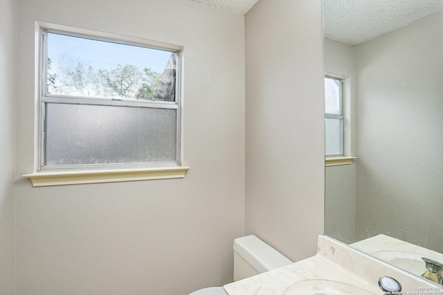 half bathroom with vanity, a wealth of natural light, a textured ceiling, and toilet