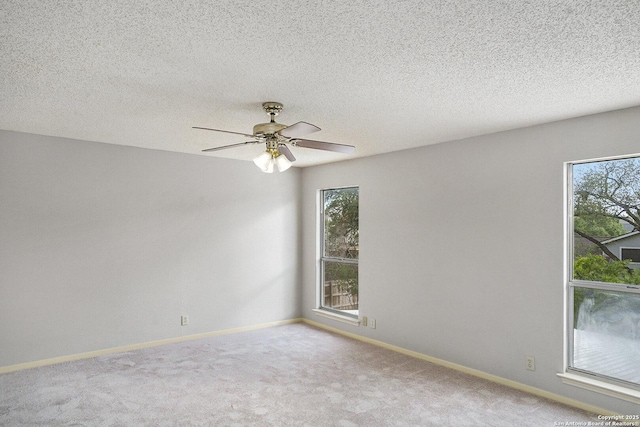 carpeted spare room featuring plenty of natural light, a ceiling fan, baseboards, and a textured ceiling
