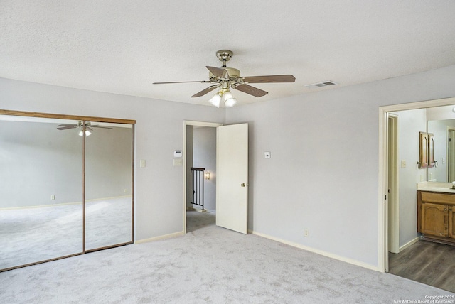unfurnished bedroom with ensuite bath, a closet, visible vents, and carpet flooring
