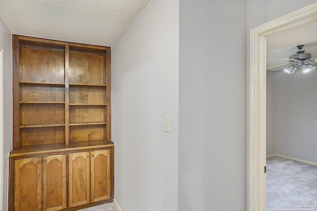 corridor with a textured ceiling, baseboards, and light carpet