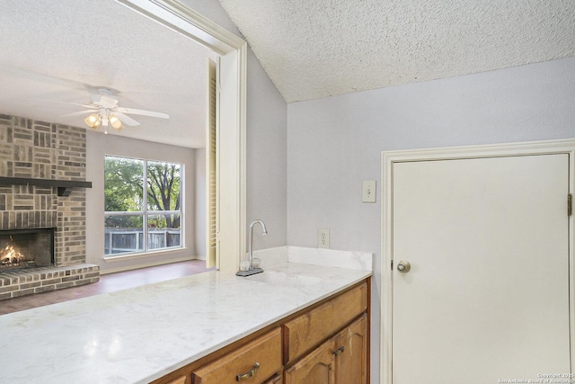 kitchen with brown cabinetry, a ceiling fan, a sink, and a textured ceiling