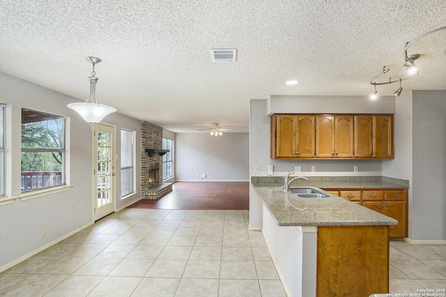 kitchen featuring a ceiling fan, a sink, brown cabinets, a peninsula, and a brick fireplace