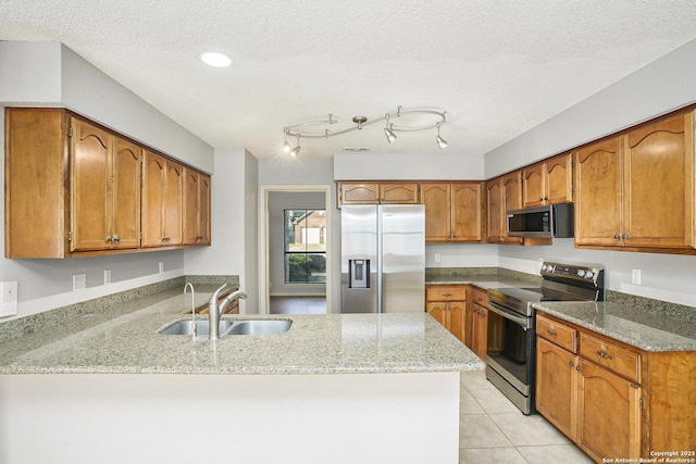 kitchen with a peninsula, appliances with stainless steel finishes, brown cabinets, and a sink