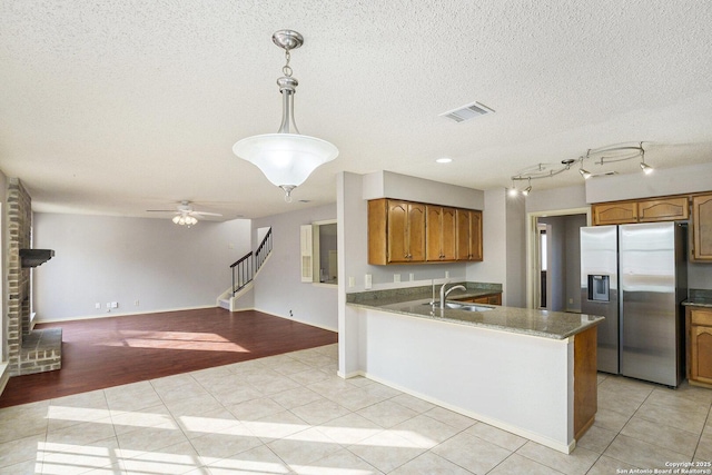 kitchen featuring brown cabinets, stainless steel refrigerator with ice dispenser, light tile patterned flooring, and a sink