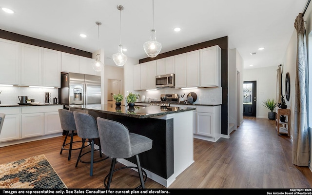kitchen with a kitchen breakfast bar, a center island, backsplash, appliances with stainless steel finishes, and wood finished floors