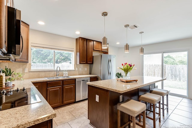 kitchen with appliances with stainless steel finishes, a breakfast bar, a sink, decorative backsplash, and a kitchen island