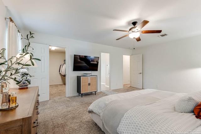 bedroom with a walk in closet, ceiling fan, visible vents, light colored carpet, and baseboards