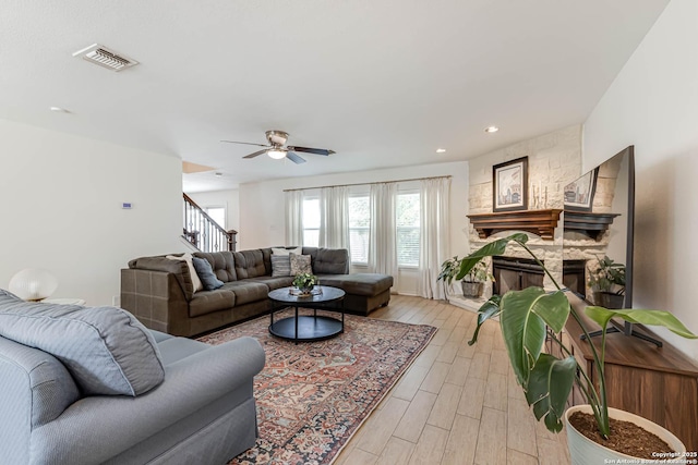 living area featuring a fireplace, light wood-style flooring, a ceiling fan, visible vents, and stairway