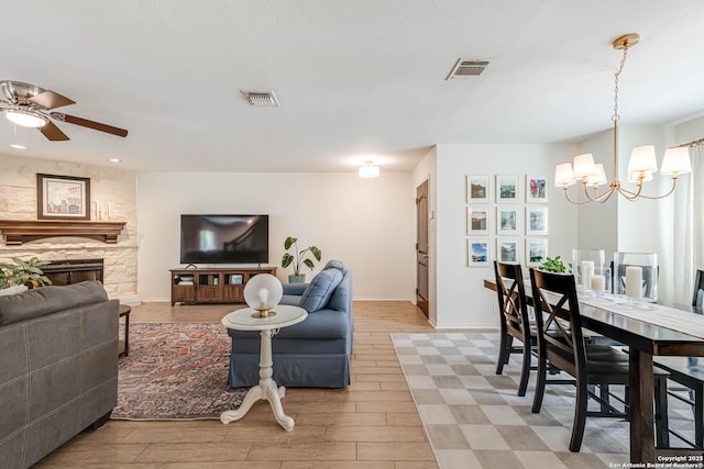 living area featuring baseboards, visible vents, ceiling fan with notable chandelier, and a fireplace