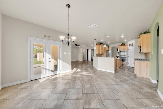 kitchen with light brown cabinetry, arched walkways, open floor plan, a notable chandelier, and appliances with stainless steel finishes