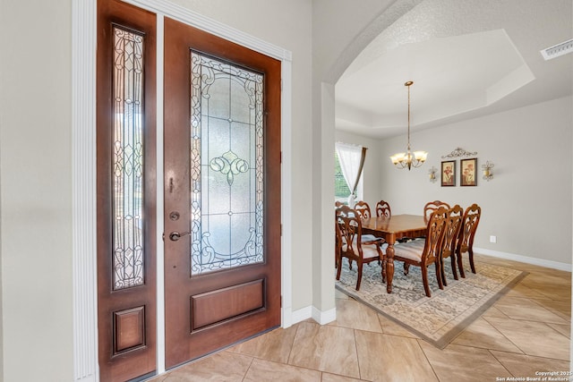 foyer featuring a tray ceiling, arched walkways, baseboards, visible vents, and a chandelier