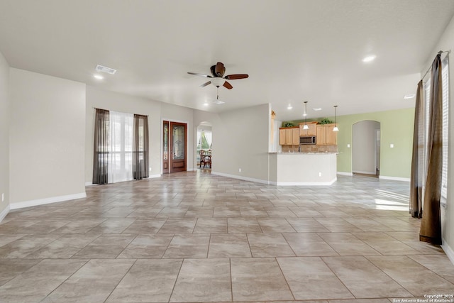 unfurnished living room with arched walkways, visible vents, baseboards, and ceiling fan