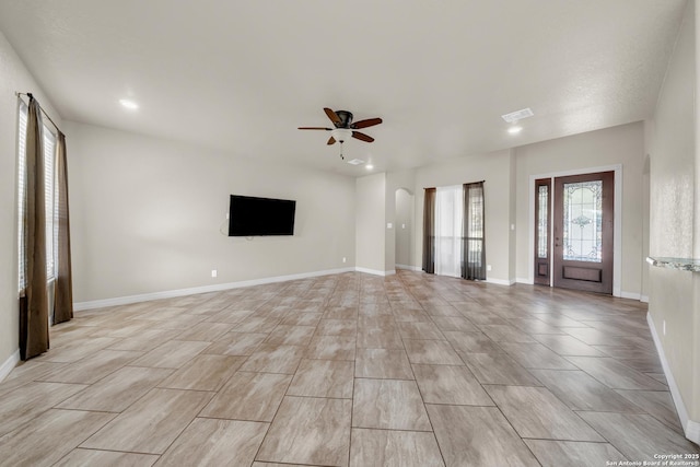 unfurnished living room featuring baseboards, a ceiling fan, visible vents, and arched walkways