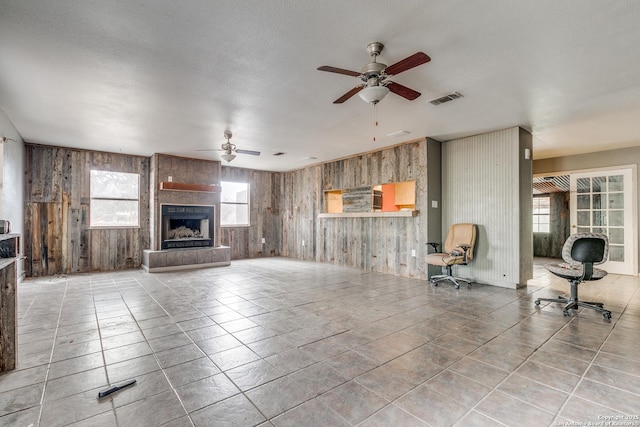 living room featuring wooden walls, a tile fireplace, visible vents, and a ceiling fan