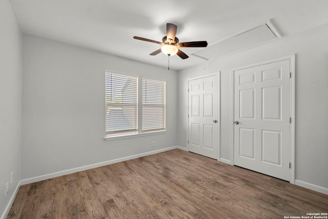unfurnished bedroom featuring attic access, ceiling fan, baseboards, and wood finished floors