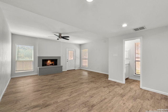 unfurnished living room with baseboards, wood finished floors, visible vents, and a warm lit fireplace