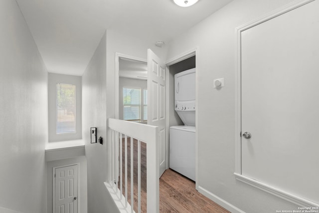 clothes washing area featuring wood finished floors, stacked washer and clothes dryer, and laundry area