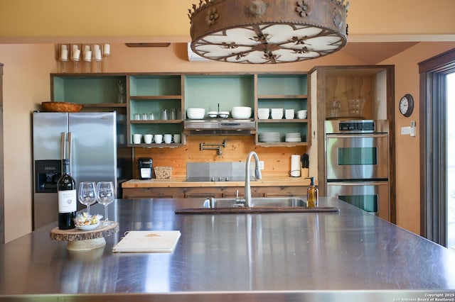kitchen with stainless steel countertops, open shelves, stainless steel appliances, and a sink
