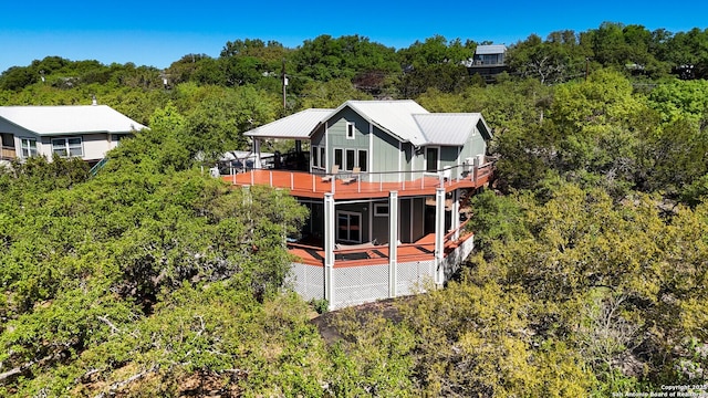 back of house with a wooden deck, a wooded view, and metal roof