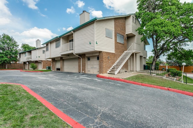 multi unit property featuring a chimney, an attached garage, brick siding, and fence