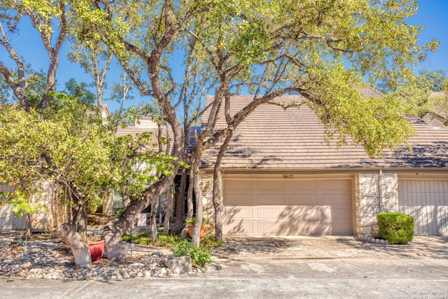 view of front of house featuring stone siding, a tile roof, driveway, and an attached garage