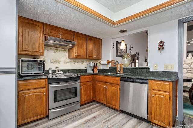 kitchen with under cabinet range hood, brown cabinetry, appliances with stainless steel finishes, and a textured ceiling