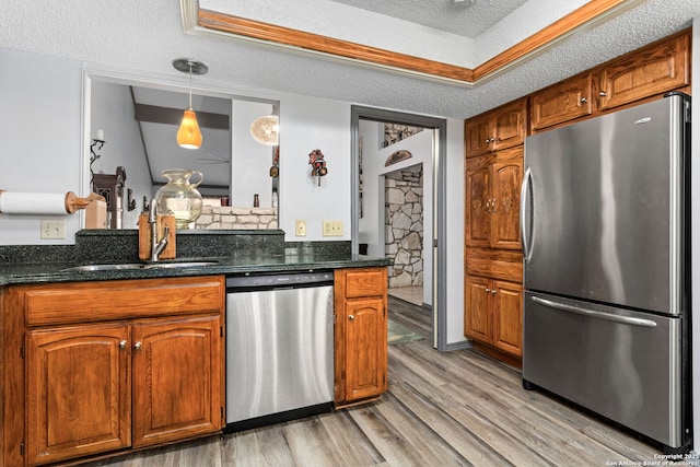 kitchen with brown cabinets, a sink, light wood-style flooring, a textured ceiling, and appliances with stainless steel finishes