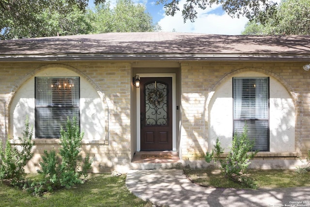 doorway to property with a shingled roof and brick siding
