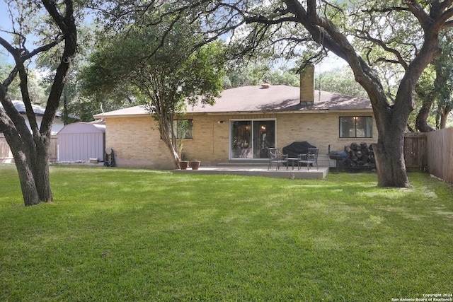 back of property with a chimney, fence, a patio, a lawn, and brick siding