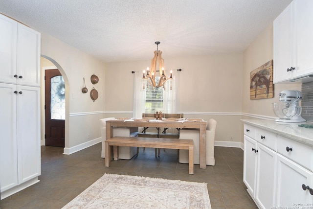 dining area with a textured ceiling, dark tile patterned floors, arched walkways, and a chandelier