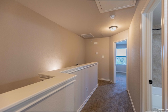 corridor featuring attic access, dark colored carpet, visible vents, baseboards, and an upstairs landing