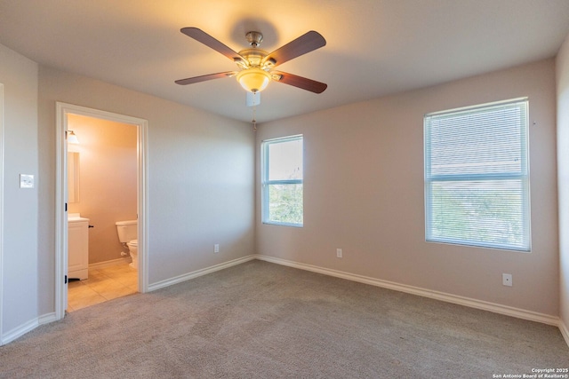 unfurnished bedroom featuring baseboards, a ceiling fan, light colored carpet, and ensuite bathroom