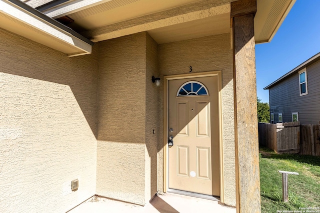 view of exterior entry with stucco siding and fence