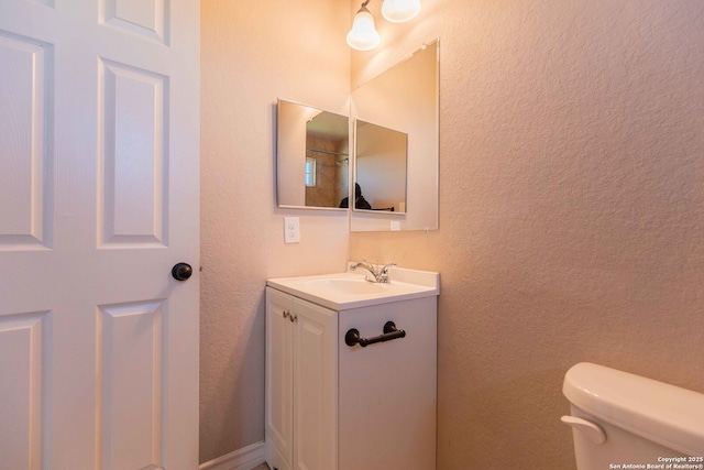 bathroom featuring a textured wall, toilet, and vanity