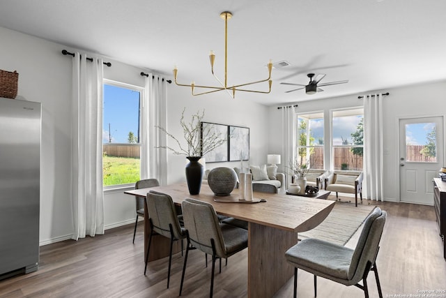 dining room with ceiling fan with notable chandelier, plenty of natural light, and wood finished floors