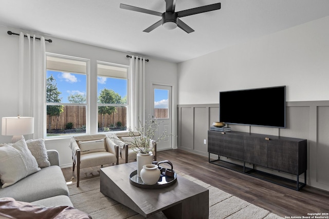 living area with a decorative wall, a ceiling fan, a wainscoted wall, and wood finished floors