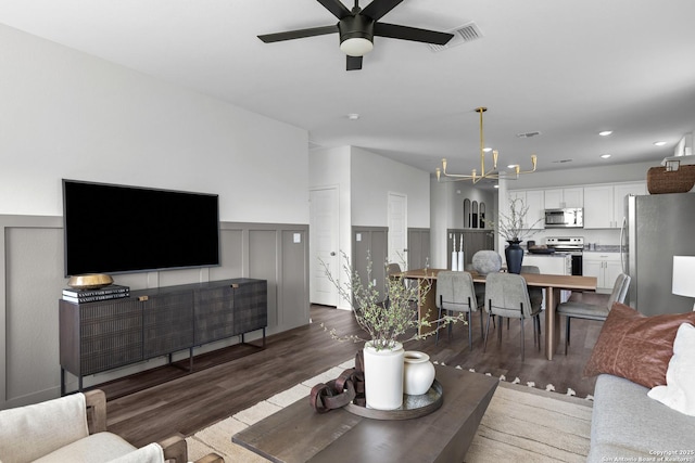living room featuring wainscoting, visible vents, recessed lighting, ceiling fan with notable chandelier, and wood finished floors