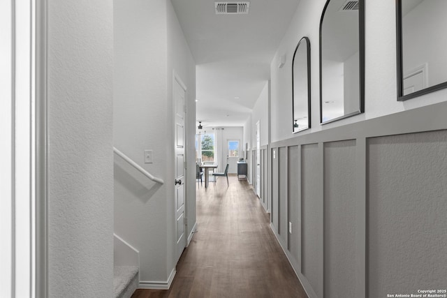 hallway featuring a textured wall, baseboards, visible vents, and dark wood-type flooring