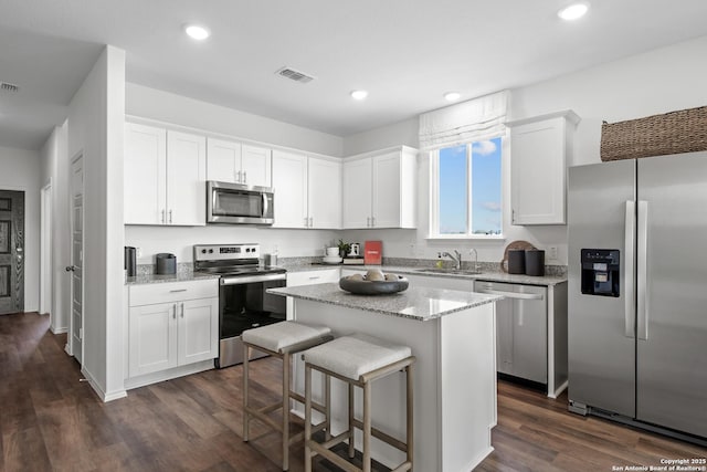 kitchen with recessed lighting, white cabinetry, a kitchen island, dark wood-type flooring, and appliances with stainless steel finishes