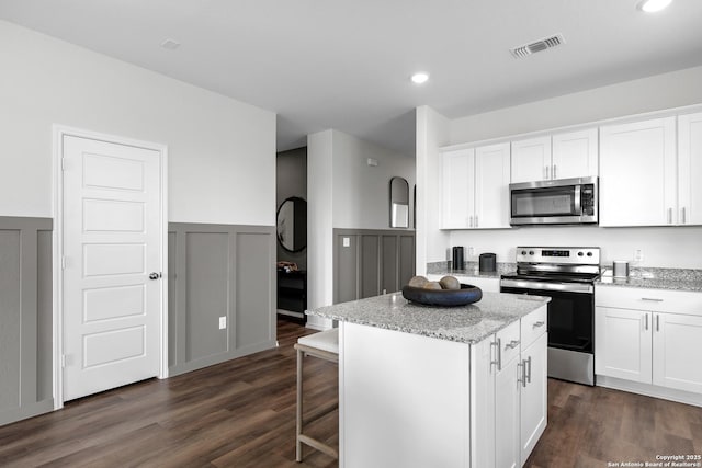 kitchen with a center island, dark wood-style floors, a wainscoted wall, visible vents, and appliances with stainless steel finishes